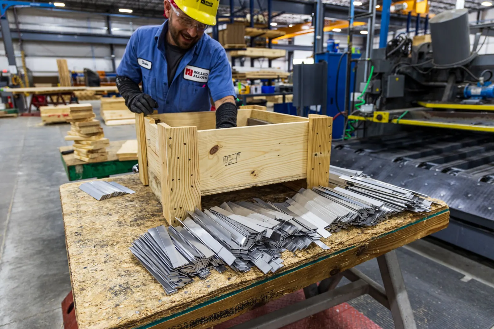 A worker in safety gear sorting metal parts in a factory