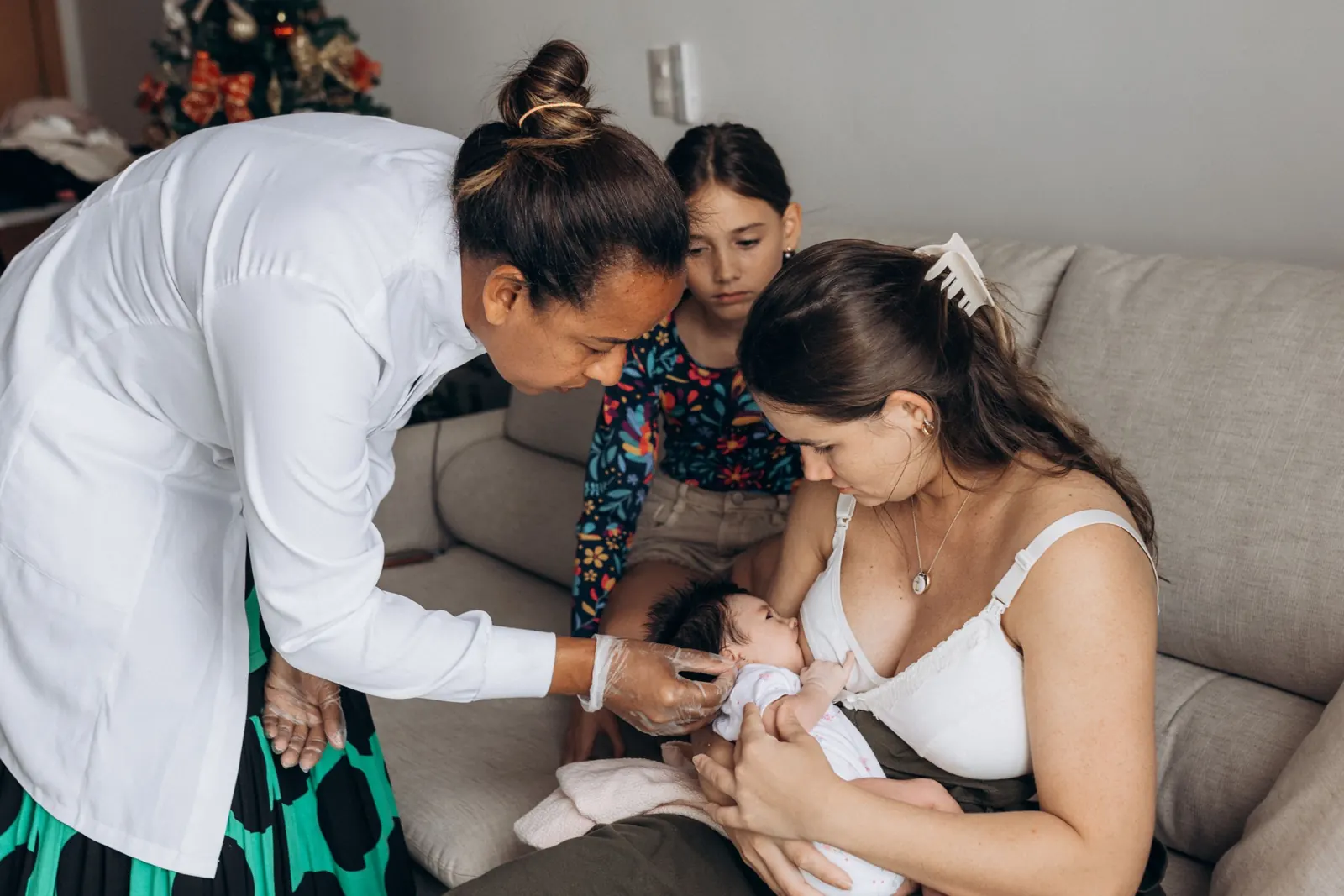 A pediatrician checking a newborn held by its mother at home
